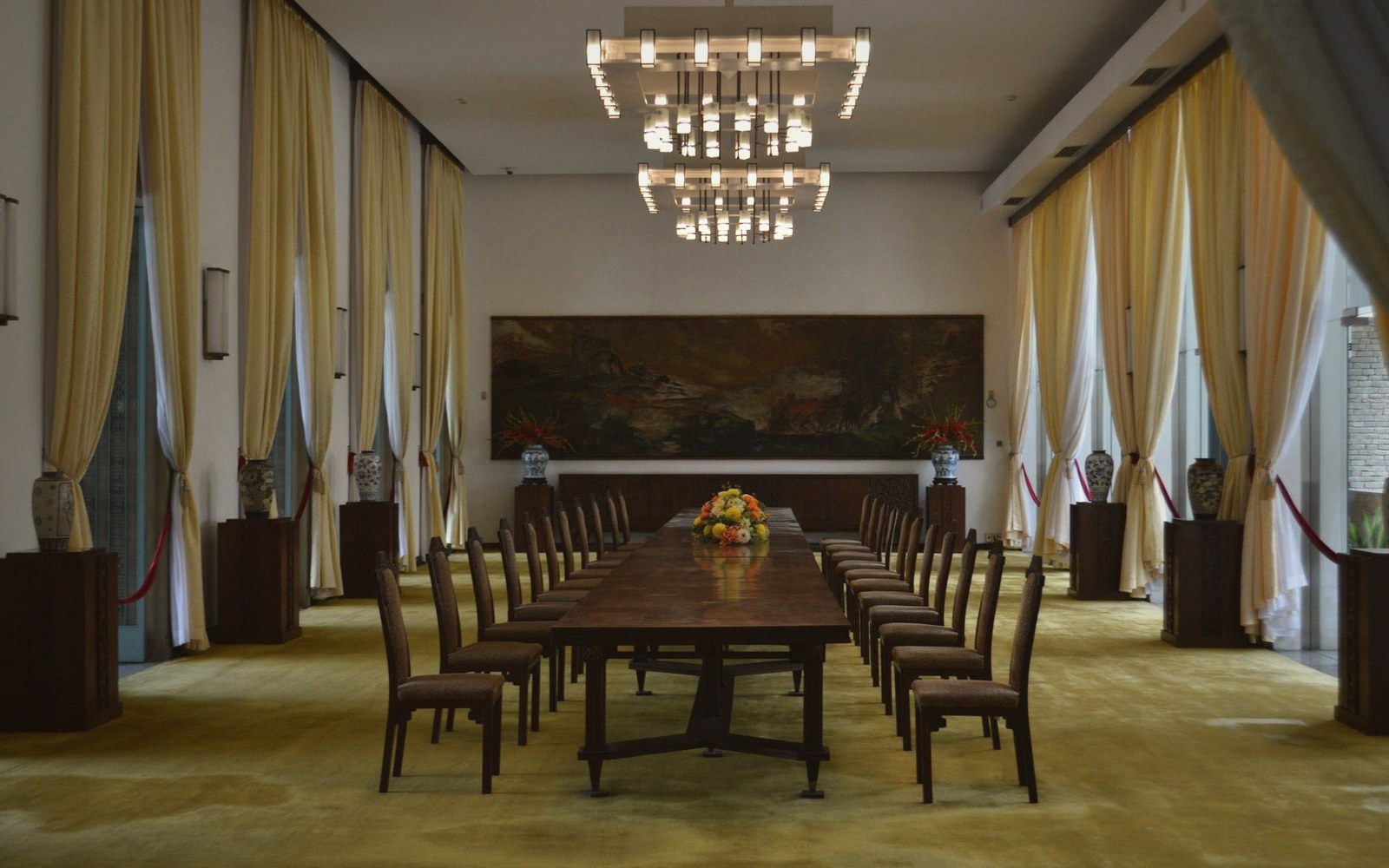 Long conference table with rows of chairs beneath a chandelier in a formal meeting hall