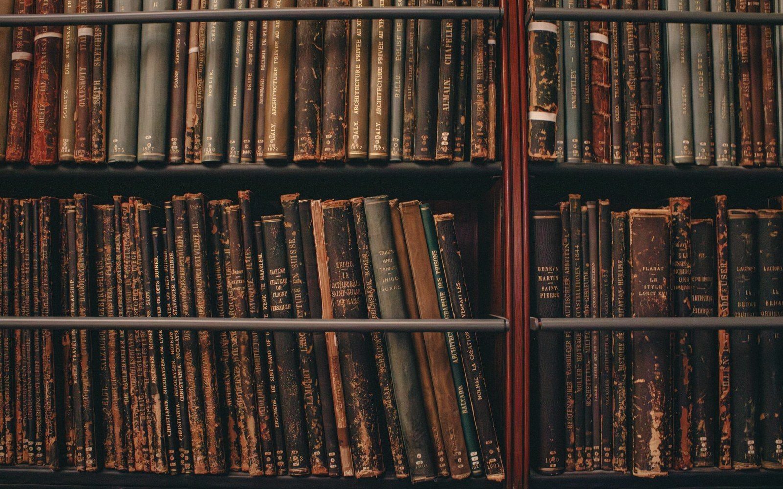 Rows of worn, leather-bound antique books packed tightly on wooden library shelves