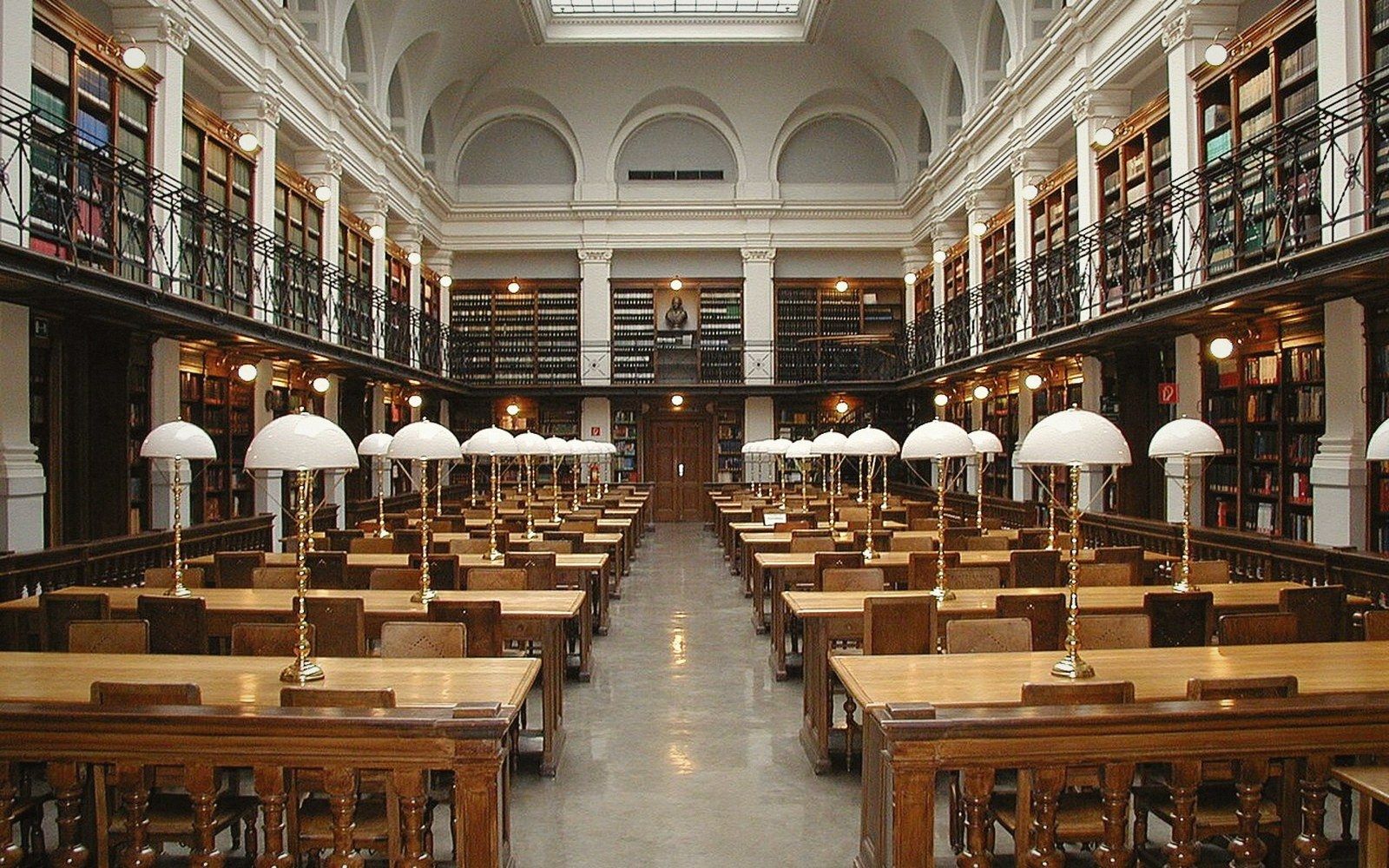 A large university reading room with a vaulted ceiling, empty desks and tall arched windows